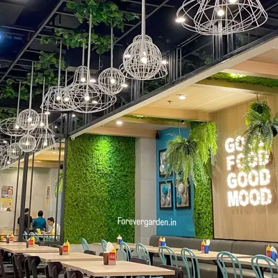 A cafe interior featuring a moss wall, hanging plants, and a "Good Food Good Mood" neon sign. This project shows how greenery can be integrated with branding to create a cohesive and inviting atmosphere.