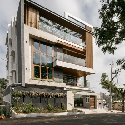 A daytime view of the Hennur Road residence, showcasing the interplay of Italian marble cladding, WPC vertical screens, and large glass windows. The design maximizes the wide frontage to create a facade that is both elegant and imposing.