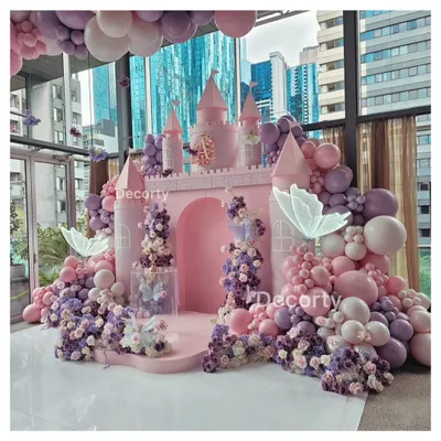 A breathtaking princess castle backdrop in shades of pink and lavender. This elaborate setup is adorned with cascading flowers, balloon garlands, and glowing butterflies, creating a real-life fairy tale for a first birthday.