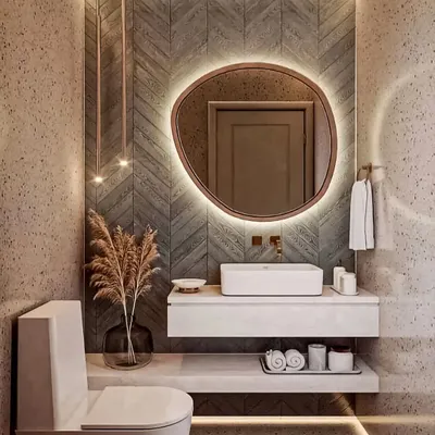 A stylish powder room featuring a floating white vanity and a uniquely shaped backlit mirror. The chevron-patterned tile wall adds texture and warmth to the space.