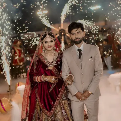 A professional photograph capturing a couple's reception entry. They are surrounded by a dense floor of white fog and framed by brilliant cold pyro sparklers, creating a high-contrast, dramatic image.