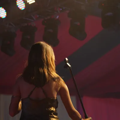 I'm facing the audience with the microphone lowered for a moment, beneath the stage lights and red-and-yellow canopy.