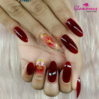 A look of pure luxury and drama. This design features long, almond-shaped nails in a deep, glossy red, with accent nails showcasing a celestial gold starburst on a sheer base.