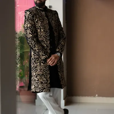 A masterpiece of fusion wear. This black sherwani is covered in dense, intricate gold floral embroidery, paired with classic white trousers for a look that is both royal and contemporary.
