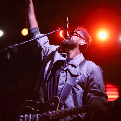 A guitarist reaching for a high note, one hand raised in sync with the music's peak. This is an action shot that freezes the climax of a song.