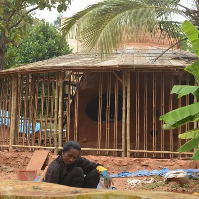 An exterior view of the Cheerville farmhouse under construction. This image shows the integration of a bamboo framework with earthen walls, showcasing a hybrid approach to sustainable building.