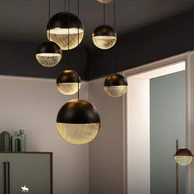 This cluster of spherical pendants features a unique dual-finish of solid black and perforated gold. The design casts a beautiful, patterned light, demonstrating where lighting becomes a form of architecture itself.