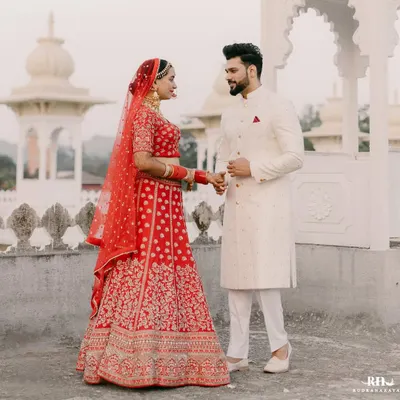 A picture of pure happiness. Our groom Abhilash looks dashing in a classic ivory sherwani, perfectly complementing the bride's vibrant red lehenga.