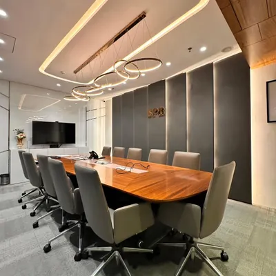 This is a full view of a boardroom designed for focus and impact. The long, polished wooden table is complemented by ergonomic chairs, while the fabric-paneled wall provides sound absorption for confidential discussions.