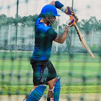 A batsman in full gear, practicing his stance in the nets. The focus is on balance, head position, and being ready to execute a powerful shot.
