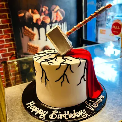 A cake worthy of a hero. This Thor-themed cake features an edible Mjolnir hammer smashing into the top, with lightning cracks and a flowing red cape made of fondant.