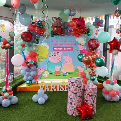 Let's jump and play with Peppa Pig! This large, colorful setup features a custom backdrop, character cutouts, and a unique balloon arrangement in shades of green, red, and blue.