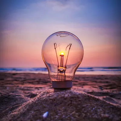 A creative sunset shot where the sun perfectly aligns with the filament of a lightbulb placed in the sand. It’s a fun illusion that makes it look like the sun is powering the bulb.