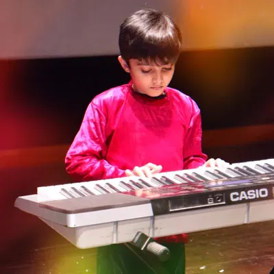 We celebrate every student's progress with opportunities to perform, like at our 'PEHAL' annual event. This moment captures a young student's focus and dedication while playing the keyboard on stage, a testament to his hard work in our music program.