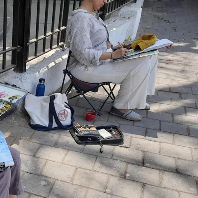 Here I am, set up on a sidewalk with my portable chair and sketchbook. This is my element, urban sketching with my local artist group, capturing the daily life of the city.