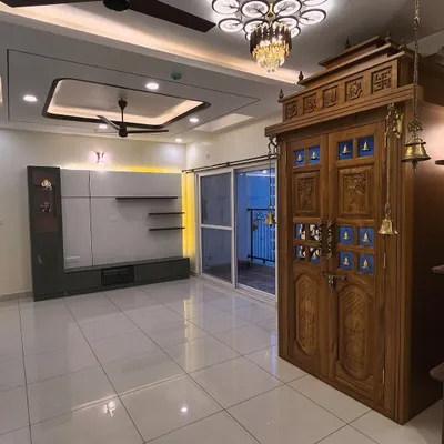 A picture-perfect view of a traditional teak wood pooja unit with carved doors and brass bells, standing next to a contemporary TV unit. This shows how we can blend different styles in one space.