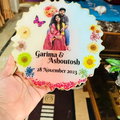 A close-up view of the personalized resin tabletop, showing the detail of the embedded flowers, butterfly graphic, and custom text. The zigzag edge adds a modern touch.