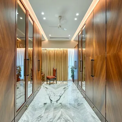 This is as grand as a walk-in wardrobe gets. We designed this expansive corridor-style closet with floor-to-ceiling wood veneer wardrobes, integrated mirrors, and a stunning book-matched marble floor.