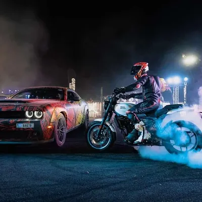 A rider performing a controlled burnout on a custom bike next to a wildly tuned Dodge Challenger. This is a signature moment from our night shows, combining dramatic smoke and lighting to create a high-impact visual for any event.