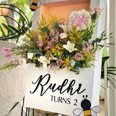 A custom welcome sign for a second birthday party with a 'Garden Party' theme. We created a beautiful shadow box filled with fresh flowers and added cute bee cutouts to match the whimsical theme.