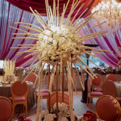 A unique and artistic centerpiece featuring a sphere of white flowers with radiating strings of pearls. This custom creation adds a dramatic and modern touch to the wedding tablescape.