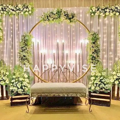 A beautiful stage setup for an engagement, featuring a golden ring backdrop adorned with white flowers and surrounded by fairy lights. The design creates a warm and magical ambiance.