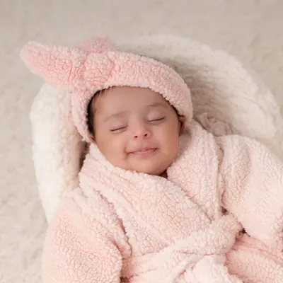 A close up of a one month old baby enjoying her "spa day". The soft pink robe and contented smile make for an adorable and unique milestone photo.