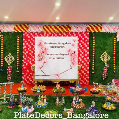 A full stage setup for a seer varisai ceremony, with a floral backdrop and a wide assortment of my decorated platters arranged neatly on a green turf.