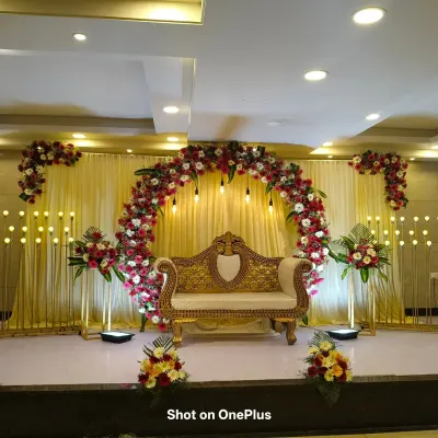 A grand reception stage decoration in Halsur. The setup features a large floral arch of red and white gerberas, a golden diwan, and rows of elegant stand-up lights on either side.