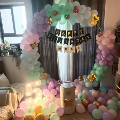 A dreamy butterfly-themed party for a 5th birthday. This cozy home setup includes a circular balloon arch in pastel pink, purple, and mint green, accented with gold butterflies and a light-up number '5'.
