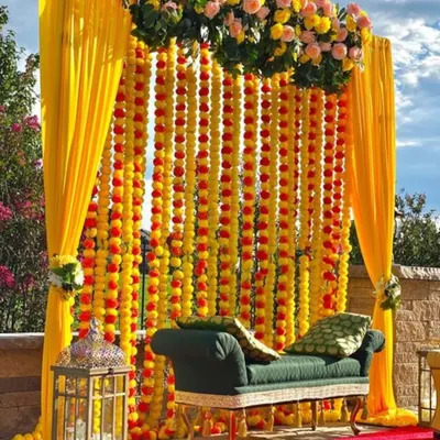 This beautiful Haldi seating arrangement is one of our signature designs. We created a full backdrop from strings of fresh marigolds, complemented by a rich green sofa for the couple. Placed outdoors under natural light, this setup provides a perfect, vibrant space for photos and ceremonies.