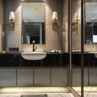 A bathroom in the Jor Bagh Residence featuring a geometric Indian stonework floor pattern. The design combines a dark marble countertop with fluted glass cabinetry and warm brass fixtures for a timelessly elegant look.