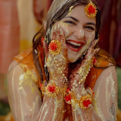 The pure, unadulterated joy of a Haldi ceremony. The bride's ecstatic expression, covered in turmeric and flowers, is absolutely priceless.