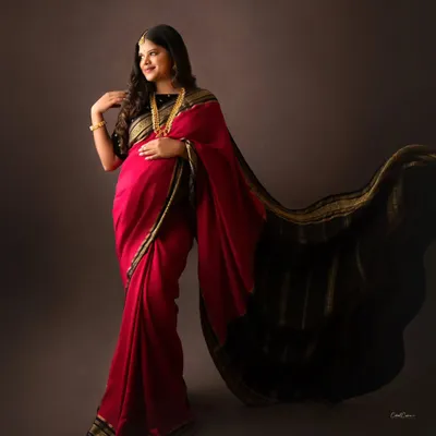 A stunning portrait of a mom-to-be in a traditional red and black saree. The flowing pallu adds a beautiful, dynamic element to the shot.
