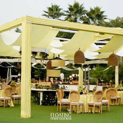 An expansive view of the 'What will you bee?' baby shower. The custom canopy with striped fabric, elegant seating arrangements, and lush greenery created a luxurious and cohesive outdoor setting.