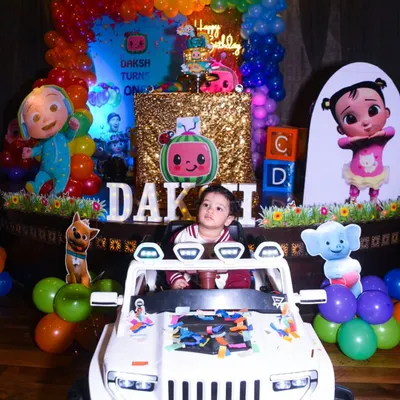 The birthday boy sits proudly in his new toy car in front of a colorful Cocomelon-themed backdrop. I capture these wide shots to show the full scale of your party decorations.