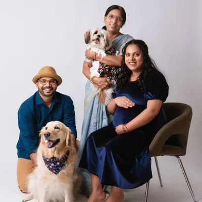 A full family portrait celebrating three generations and the furry family members. The expecting couple is joined by a grandparent and their two dogs for a memorable studio maternity photo.