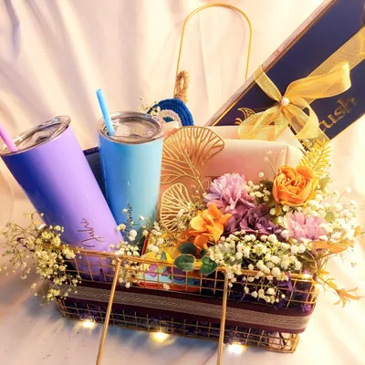 A vibrant and colorful wedding gift hamper for a fun-loving couple. This basket includes two personalized tumblers, a jewelry box, and other goodies, all surrounded by a beautiful floral arrangement.
