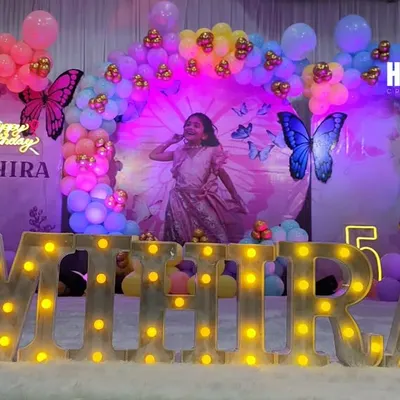 This butterfly-themed birthday party was a dream to create. I designed a magical backdrop with a photo of the birthday girl, surrounded by a rainbow balloon arch and floating butterflies, with her name "MIHIRA" lit up in large marquee letters.