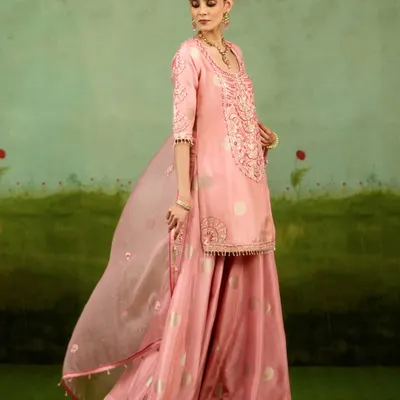 This playful yet refined sharara set in soft pink showcases fluid lines and hand-finished detail. The sheer dupatta adds a touch of grace, making it perfect for a daytime festive event.