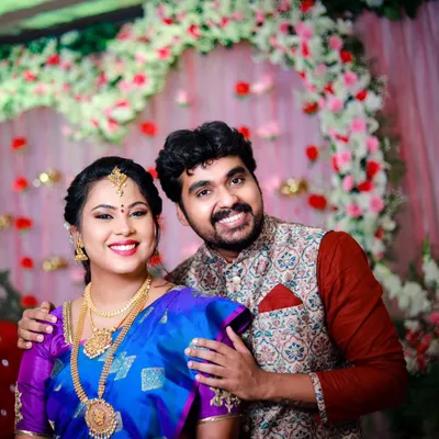A happy couple portrait from an engagement ceremony. The vibrant floral backdrop and their joyful smiles perfectly capture the celebratory mood.