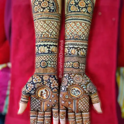 A complete engagement henna design extending up the forearms. This piece includes personalized portraits, floral bands, lotus motifs, and detailed gridwork for a breathtaking result.