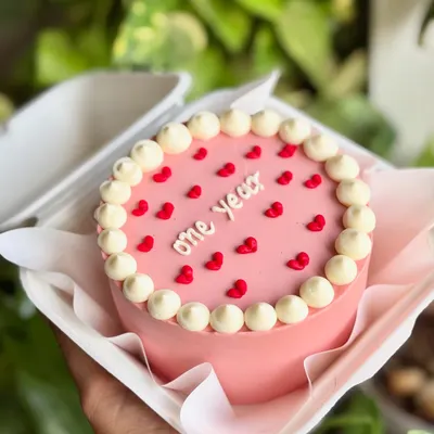 A tiny cake for a big milestone. This pink bento cake celebrates "one year" with a classic pearl border and tiny red hearts, packed and ready to gift.
