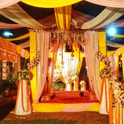 A stunning outdoor evening mandap with a ceiling of draped yellow and pink fabric, illuminated by a central chandelier and floral arrangements.