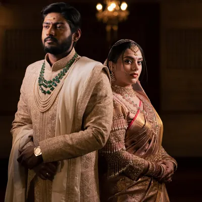 A powerful and regal portrait of a couple on their wedding day. The dramatic, low-key lighting emphasizes their stunning traditional attire and their strong, united presence.