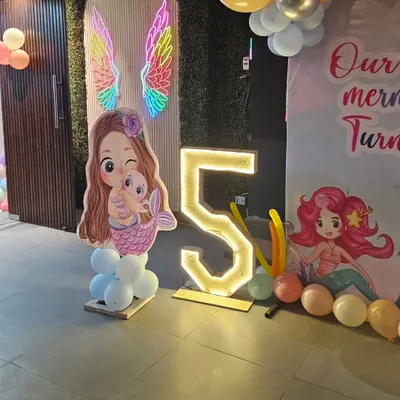 A magical mermaid theme for a 5th birthday, complete with a mermaid cutout, a light-up number "5", and colorful neon angel wings.