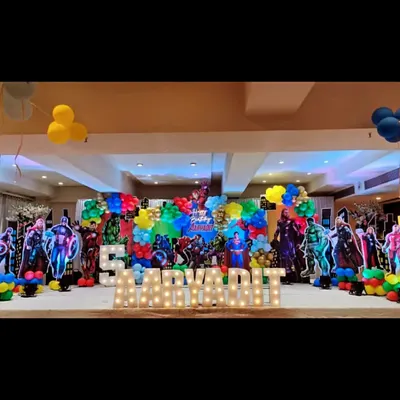 An epic superhero assembly for a 5th birthday party. The stage is packed with cutouts of famous heroes, colorful balloon clusters, and the birthday boy's name in large marquee letters, creating a powerful and exciting atmosphere.