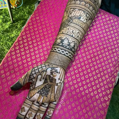 A full arm bridal mehendi featuring a detailed portrait of a groom. The design incorporates traditional Rajasthani architecture and peacock motifs.