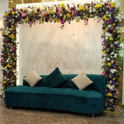 A modern and chic engagement backdrop. The rectangular arch is covered in a mix of colorful flowers, perfectly framing the stylish teal velvet sofa for photos.