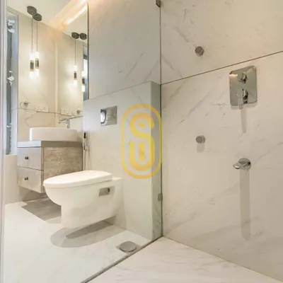 A bright and minimalist bathroom design using white marble-patterned tiles. The space features a wall-mounted toilet and a floating vanity to maximize floor space, with a glass partition for the shower area.